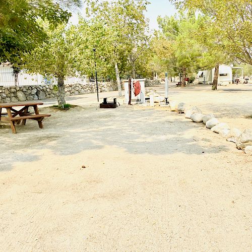 An outdoor area with trees, a picnic table, pathway, and some stone decorations. There is a clothesline with a red item hanging in the background.