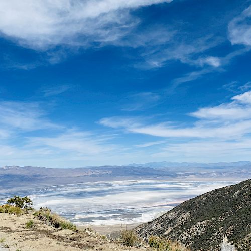 The image shows a scenic landscape with mountains, a valley, and a partly cloudy sky. The view showcases natural beauty and wide-open spaces.