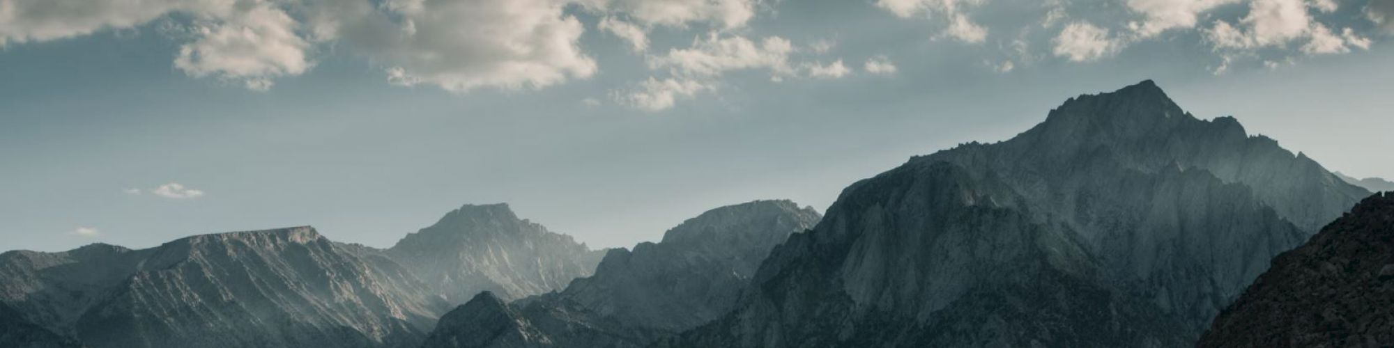 A stunning mountain range under a partly cloudy sky, with light breaking through, illuminating parts of the rugged terrain, creating a serene landscape.