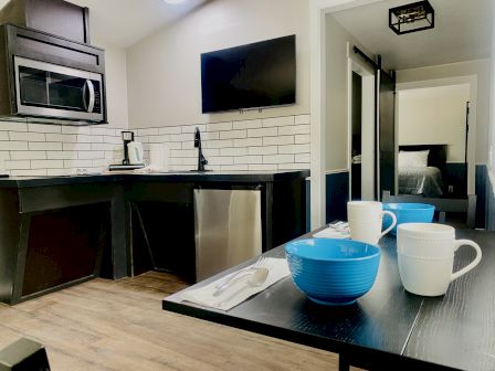 Modern kitchenette with stainless appliances, white subway tile, and small dining table set with blue bowls and white mugs.