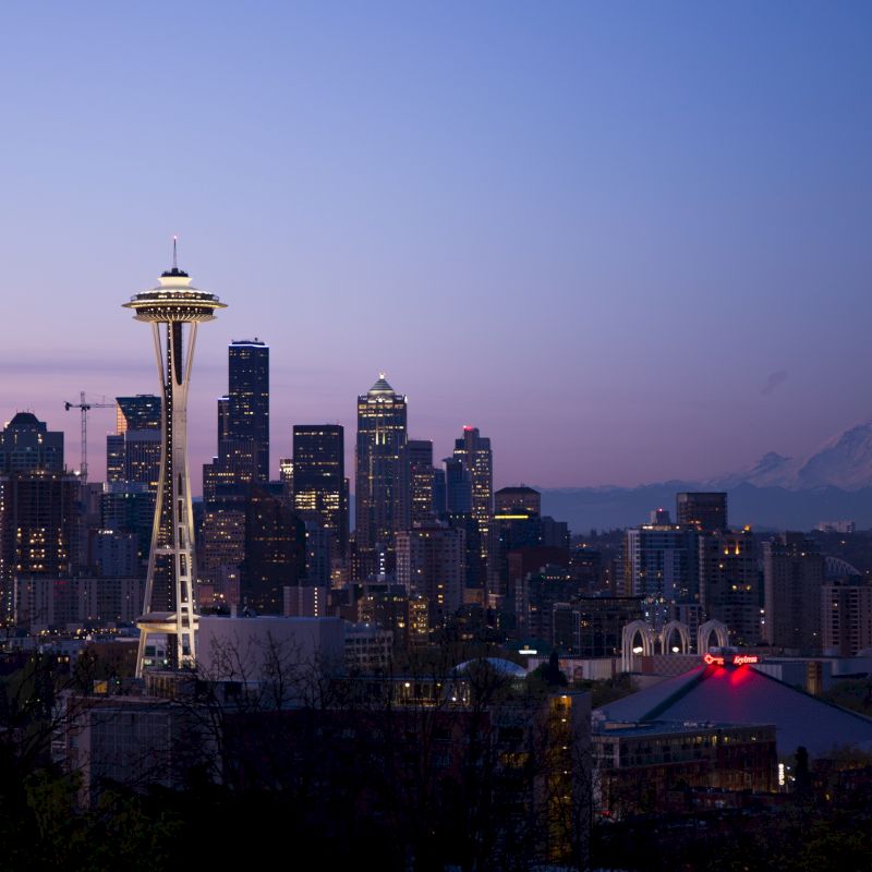 This image shows the Seattle skyline at dusk, featuring the Space Needle prominently with Mount Rainier in the background under a clear sky.