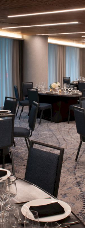 A modern dining area set up with round tables, black chairs, elegant table settings, and decorative candles, illuminated by overhead lighting.
