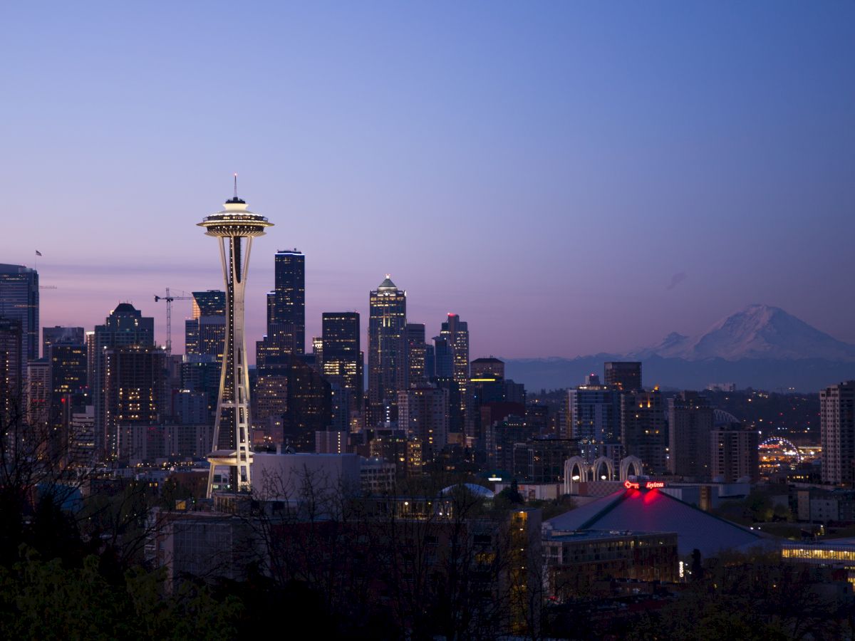 The image showcases the Seattle skyline at dusk, prominently featuring the Space Needle with tall buildings in the background and Mount Rainier visible.