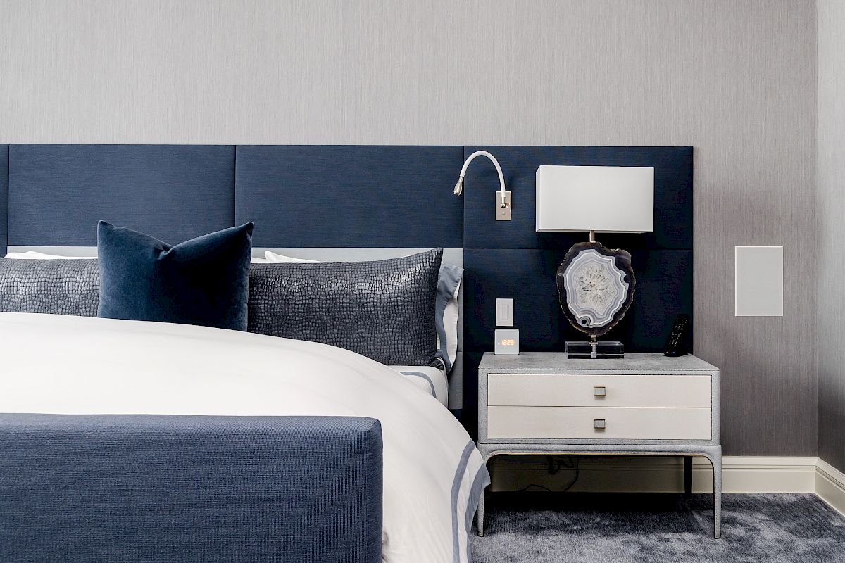 This image features a modern bedroom with a blue and white color scheme, including a bed and nightstand with a lamp and decorative items.