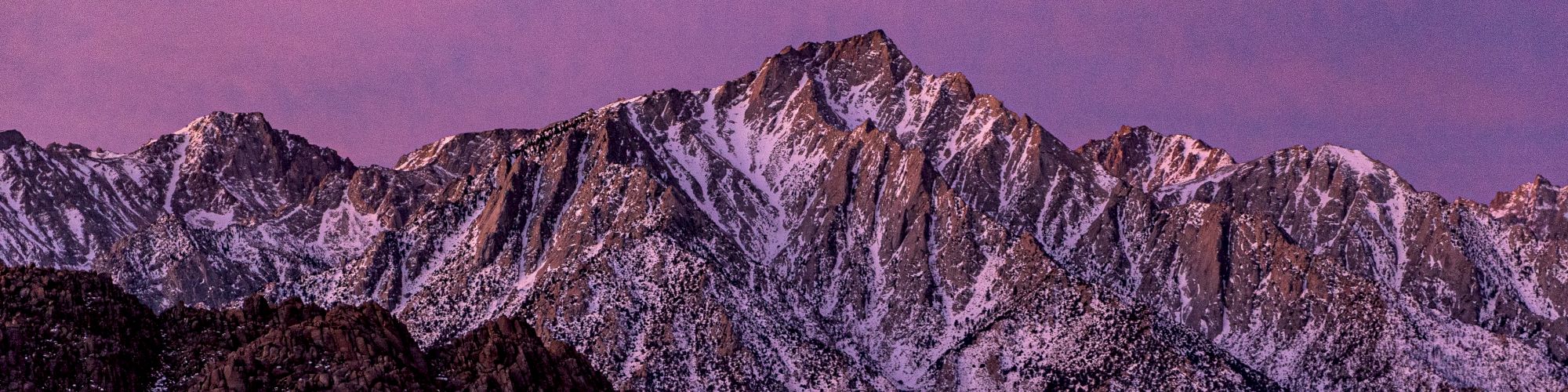 A mountain range with snow-capped peaks is under a purple sky, showing rugged terrain and beautiful snowy textures.