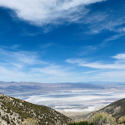 A scenic landscape features a mountainous foreground and a vast, dry salt flat under a bright blue sky with scattered clouds.