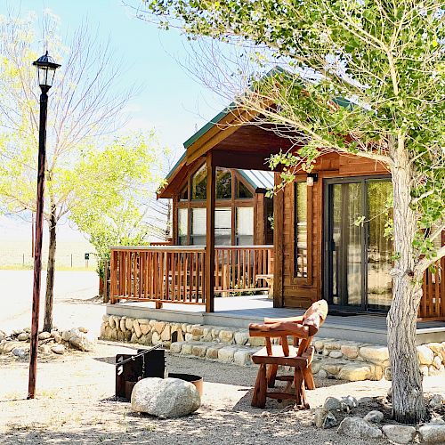 A rustic cabin with a porch, surrounded by trees, with a wooden chair and a street lamp in the foreground.