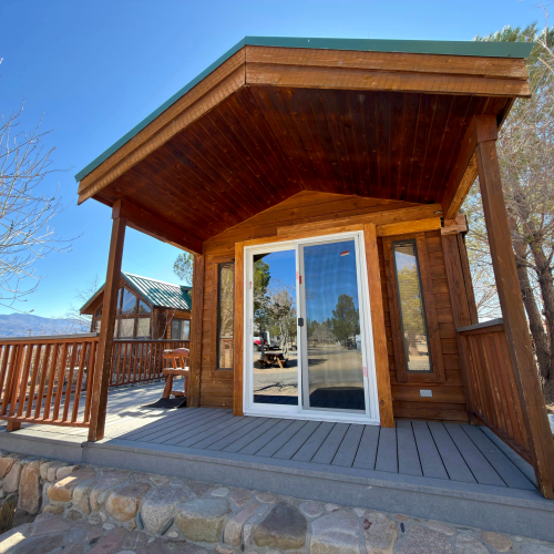 A cozy wooden cabin with a slanted roof, a glass front door, and a small porch overlooking a scenic desert landscape.