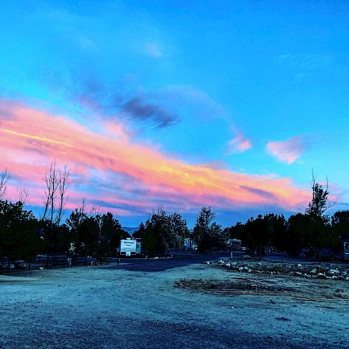 A colorful sunset sky with pink and blue hues over a rural area with trees and a dirt road.